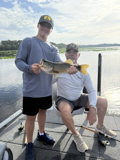 Two anglers with a largemouth bass aboard the boat